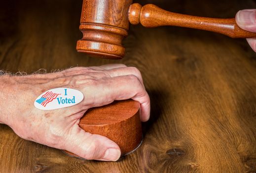 I voted campaign sticker on senior hand with mallet and gavel to illustrate the concept of judges overruling the rights of voters in the election
