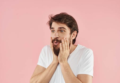 Emotional man holds his hand near his face on a pink background Copy Space. High quality photo