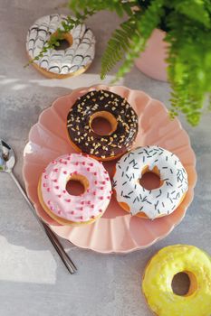 Sweet and fresh colored different donuts with chocolate frosted, glazed and sprinkles, icing topping on pink plate on concrete background.