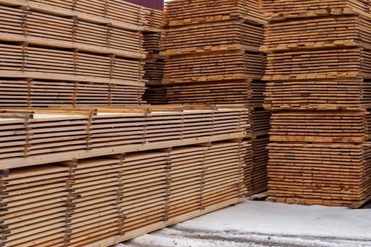 Large stacks of wooden boards background with inear perspective. Winter woodwork industrial storage.