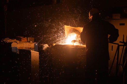 steelworker removing slag from steel furnace with sparks and smoke exhaust.