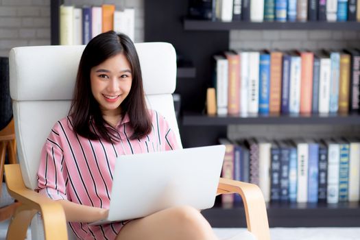 Beautiful of portrait asian young woman freelance working online laptop sitting on chair at living room, girl using notebook computer with connect to internet for distance job, business and success concept.