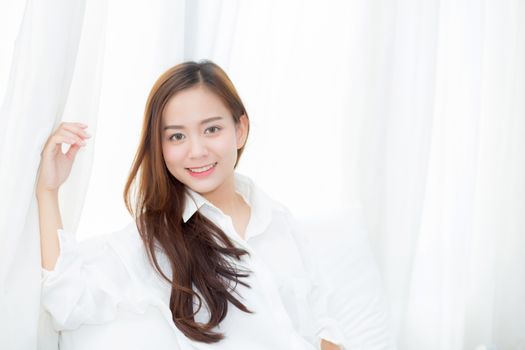 Portrait of beautiful young asian woman standing the window and smile while wake up with sunrise at morning, lifestyle and relax concept.