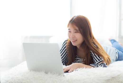 Beautiful of portrait asian young woman lying on bed using laptop at bedroom for leisure and relax, freelance with girl working notebook, communication concept.