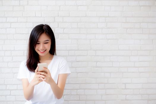 Beautiful of portrait young asian woman touch phone and smile standing on cement brick background, freelance female calling telephone, communication concept.