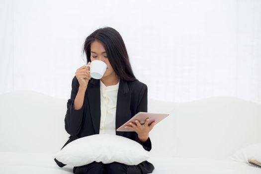 Beautiful of portrait young asian businesswoman sitting on sofa at home looking tablet computer and drinking coffee, woman ralex with internet, communication and business concept.