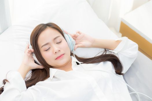 Beautiful asian young woman enjoy listen music with headphone while lying in bedroom, relax girl with earphone internet online, leisure and technology concept.