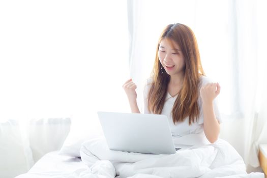 Beautiful happiness young asian woman using laptop work with success on bed in the home, girl and notebook shopping online with glad, communication concept.