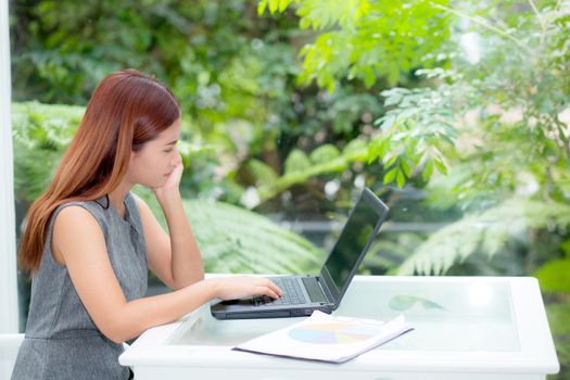 Beautiful of portrait asian young woman working online on laptop computer with graph paper sitting at office, professional female freelancer using notebook with connect to internet for distance job, business concept.