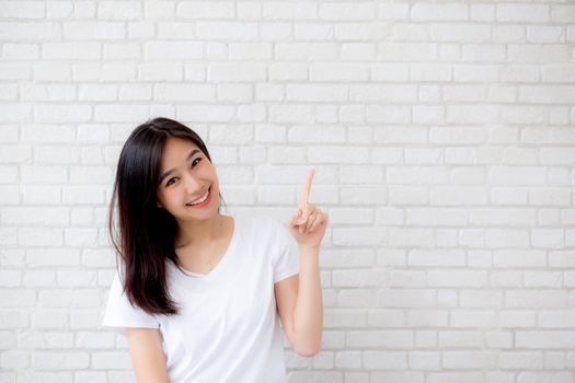 Portrait of beautiful young asian woman happiness standing finger pointing something on gray cement texture grunge wall brick background, businesswoman is a smiling on concrete, business people concept.