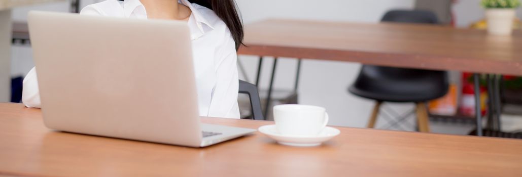 Closeup banner website asian young woman working online on laptop sitting at coffee shop, professional female freelancer using notebook computer with connect to internet for distance job.