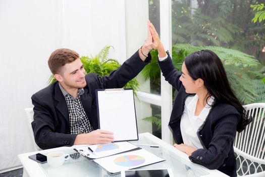 Team businesspeople hi five touching hand man and woman with smiling meeting for celebration at office, business marketing success with teamwork and graph on table.