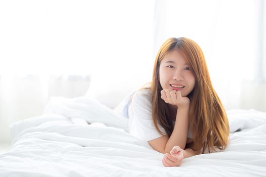 Beautiful portrait young asian woman lying and smile while wake up with sunrise at morning, lifestyle and relax concept.