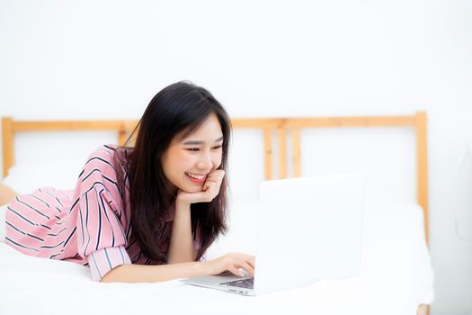 Beautiful asian young woman lying on bed using laptop at bedroom for leisure and relax, freelance with girl working notebook, communication concept.