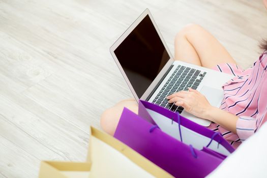 Closeup asian woman shopping online with laptop computer sitting on floor on room, girl holding credit card purchase and shopping bags, lifestyle concept.