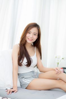 Portrait beautiful young asian woman sitting and smile the window at bedroom while wake up with sunrise at morning, lifestyle and relax concept.