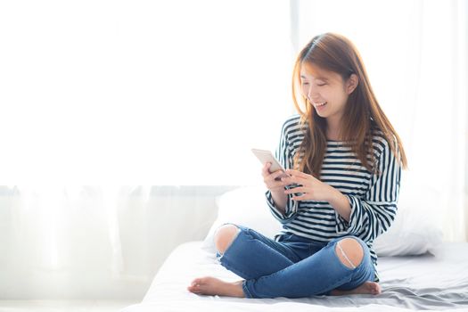 Beautiful young asian woman smiling sitting relax on the bed in the morning, girl using mobile smart phone talking enjoy, communication and social network concept.