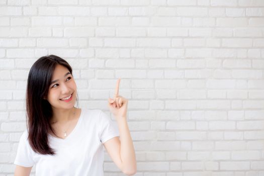 Portrait of beautiful young asian woman happiness standing finger pointing something on gray cement texture grunge wall brick background, businesswoman is a smiling on concrete, business people concept.