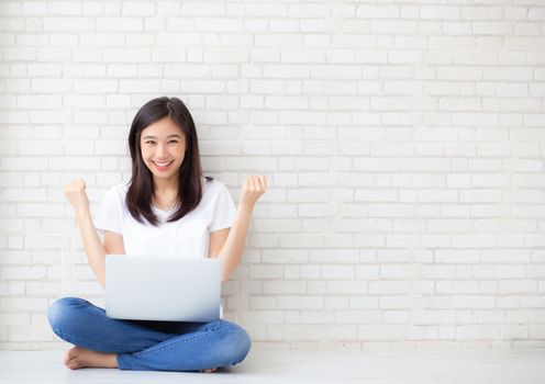 Beautiful of portrait asian young woman excited and glad of success with laptop computer, girl sitting working on cement brick background, career freelance business concept.