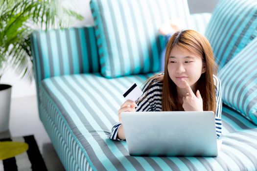 Beautiful of portrait young asian woman lying think use credit card with laptop, Content girl shopping online and payment with notebook computer on sofa, lifestyle concept.