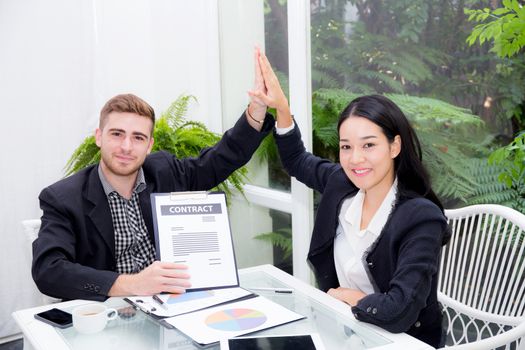 Team businesspeople hi five touching hand man and woman with smiling meeting for celebration at office, business marketing success with teamwork and graph on table.