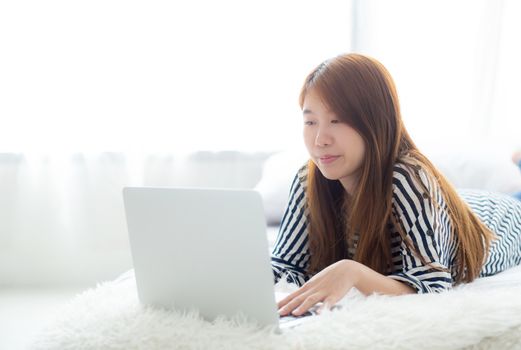 Beautiful of portrait asian young woman lying on bed using laptop at bedroom for leisure and relax, freelance with girl working notebook, communication concept.