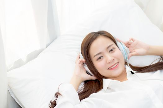Beautiful asian young woman enjoy listen music with headphone while lying in bedroom, relax girl with earphone internet online, leisure and technology concept.
