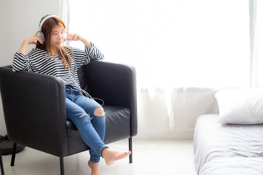 Beautiful asian young woman enjoy and fun listen music with headphone sitting on chair in the bedroom, girl relax with earphone, leisure and technology concept.