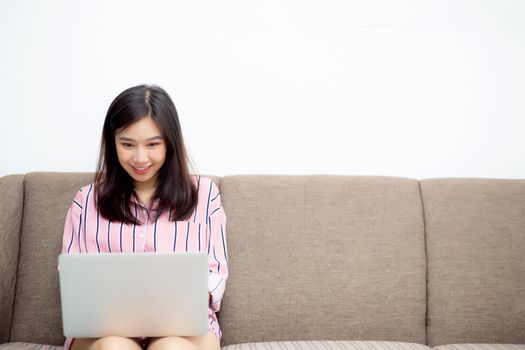 Beautiful of portrait asian young woman working online laptop sitting on sofa at living room, girl using notebook computer with connect to internet for distance job, business and success concept.