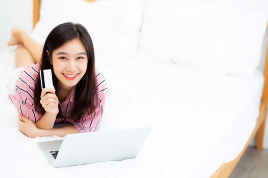 Beautiful portrait young asian woman lying users credit card with laptop, Content girl shopping online and payment with notebook computer on bed, lifestyle concept.