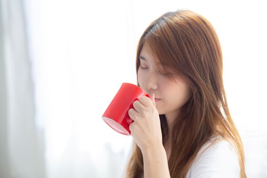 Beautiful of portrait young asian woman with drink acup of coffee standing curtain window background in bedroom, girl relax in morning at home, lifestyle concept.