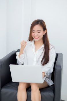 Beautiful of portrait happy young asian woman using laptop work with success on chair in the home, girl and notebook shopping online with glad, communication concept.