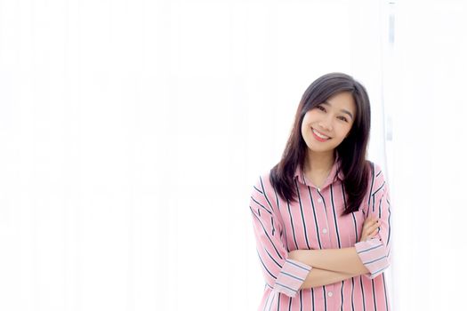 Portrait of beautiful young asian woman standing the window and smile while wake up with sunrise at morning, lifestyle and relax concept.