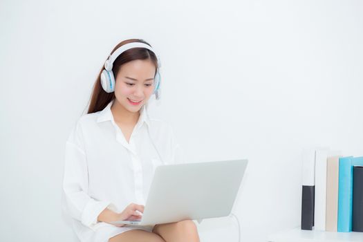 Beautiful young asian woman relax with wear headphone enjoy listening music using laptop computer, girl working laptop on chair in the living room, communication and lifestyle concept.