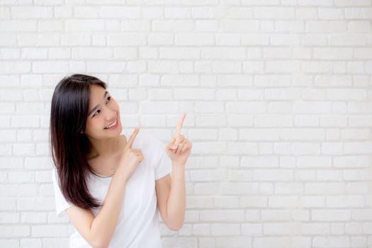 Portrait of beautiful young asian woman happiness standing finger pointing something on gray cement texture grunge wall brick background, businesswoman is a smiling on concrete, business people concept.