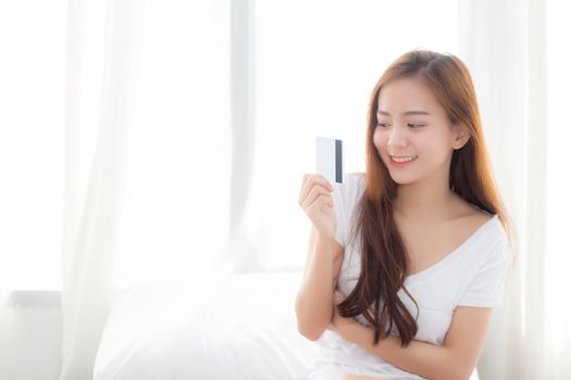 Beautiful portrait young asian woman shopping online with credit card sitting in bedroom, girl with customer purchase of payment online, lifestyle concept.