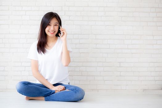 Beautiful of portrait young asian woman talk smart phone and smile sitting on cement concrete brick background, freelance female calling telephone, communication of mobile concept.