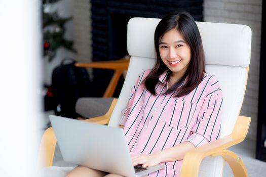 Beautiful of portrait asian young woman working online laptop with smile and happy sitting on chair at living room, girl using notebook computer with connect to internet, business and success concept.
