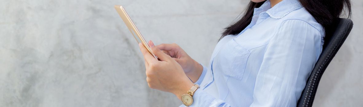 Closeup banner website young asian woman touching tablet computer sitting on concrete cement background, freelancer female calling telephone, communication concept.