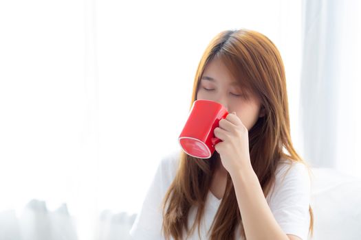 Beautiful of portrait young asian woman with drink acup of coffee standing curtain window background in bedroom, girl relax in morning at home, lifestyle concept.