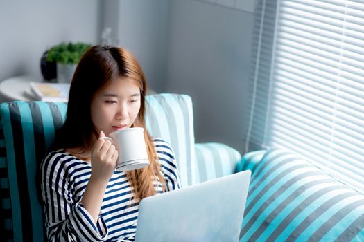 Beautiful of portrait young asian woman sitting use credit card with laptop and drink coffee, Content girl shopping online and payment with notebook computer on sofa, lifestyle concept.