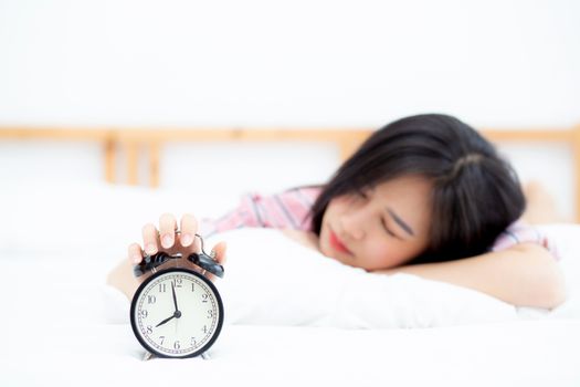 Beautiful asian young woman turn off alarm clock in morning, wake up for sleep with alarm clock, relax and lifestyle concept.