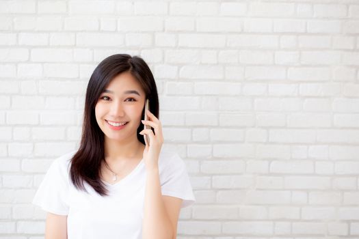 Beautiful of portrait young asian woman talk smart phone and smile standing on cement brick background, freelance female calling telephone, communication of mobile concept.