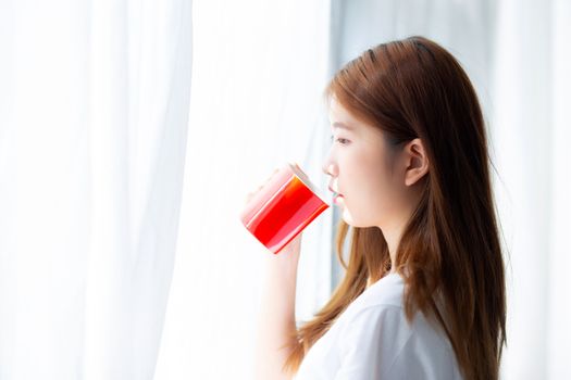 Beautiful of portrait young asian woman with drink acup of coffee standing curtain window background in bedroom, girl relax in morning at home, lifestyle concept.
