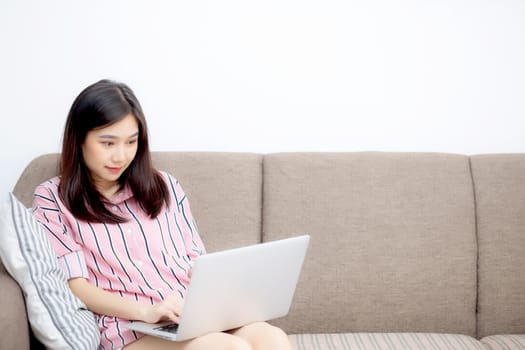 Beautiful of portrait asian young woman working online laptop with smile and happy sitting on sofa at living room, girl using notebook computer with connect to internet, business and success concept.
