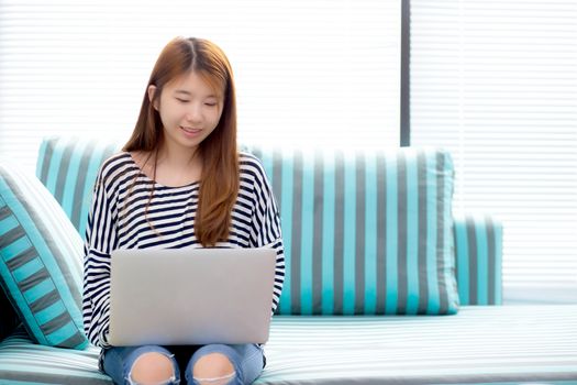 Beautiful of portrait asian young woman working online laptop sitting on sofa at living room, girl using notebook computer with connect to internet, business and success concept.