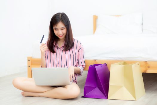 Beautiful of asian woman shopping online with laptop computer sitting on floor on room, girl holding credit card purchase and shopping bags, lifestyle concept.
