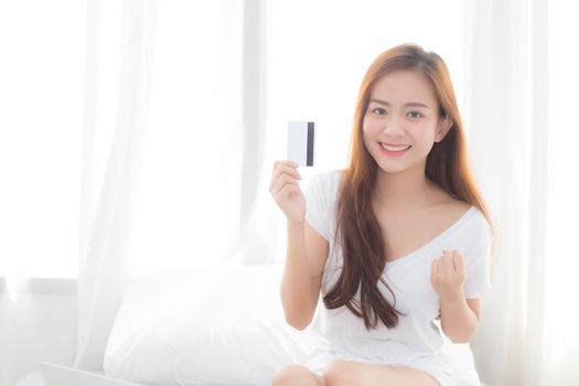 Beautiful portrait young asian woman shopping online with credit card sitting in bedroom, girl with customer purchase of payment online, lifestyle concept.
