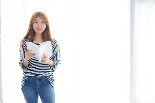 Beautiful of portrait young asian woman relax standing reading book on bedroom at home, girl study literature, education and lifestyle concept.