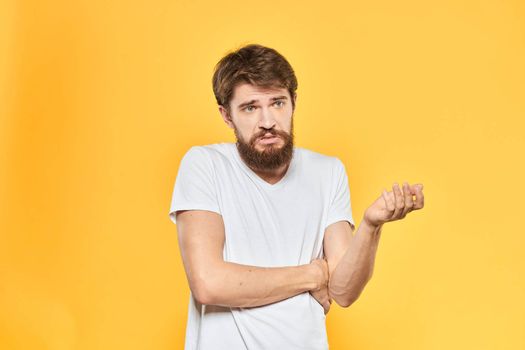 Bearded man in a white T-shirt gestures with his hands emotions studio yellow background. High quality photo